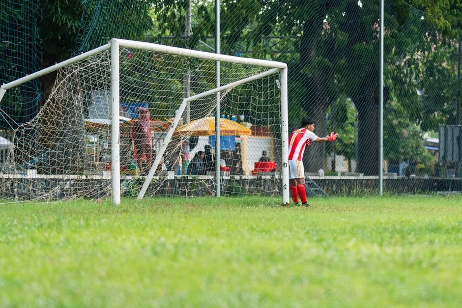 한 어린 축구 선수가 낮 시간에 야외 경기장에서 골대를 지키며 경기를 펼치고 있다.